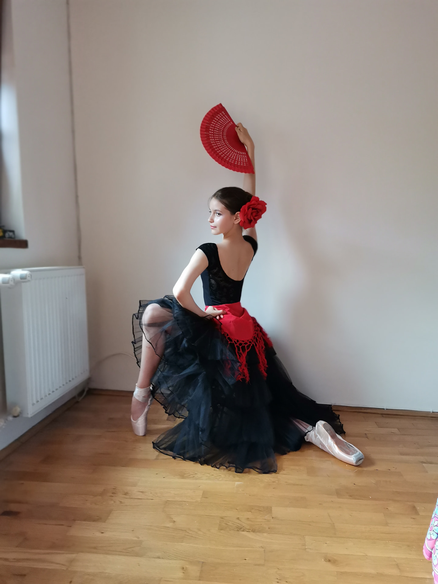 Tânără balerină în costum negru, cu floare și evantai roșu